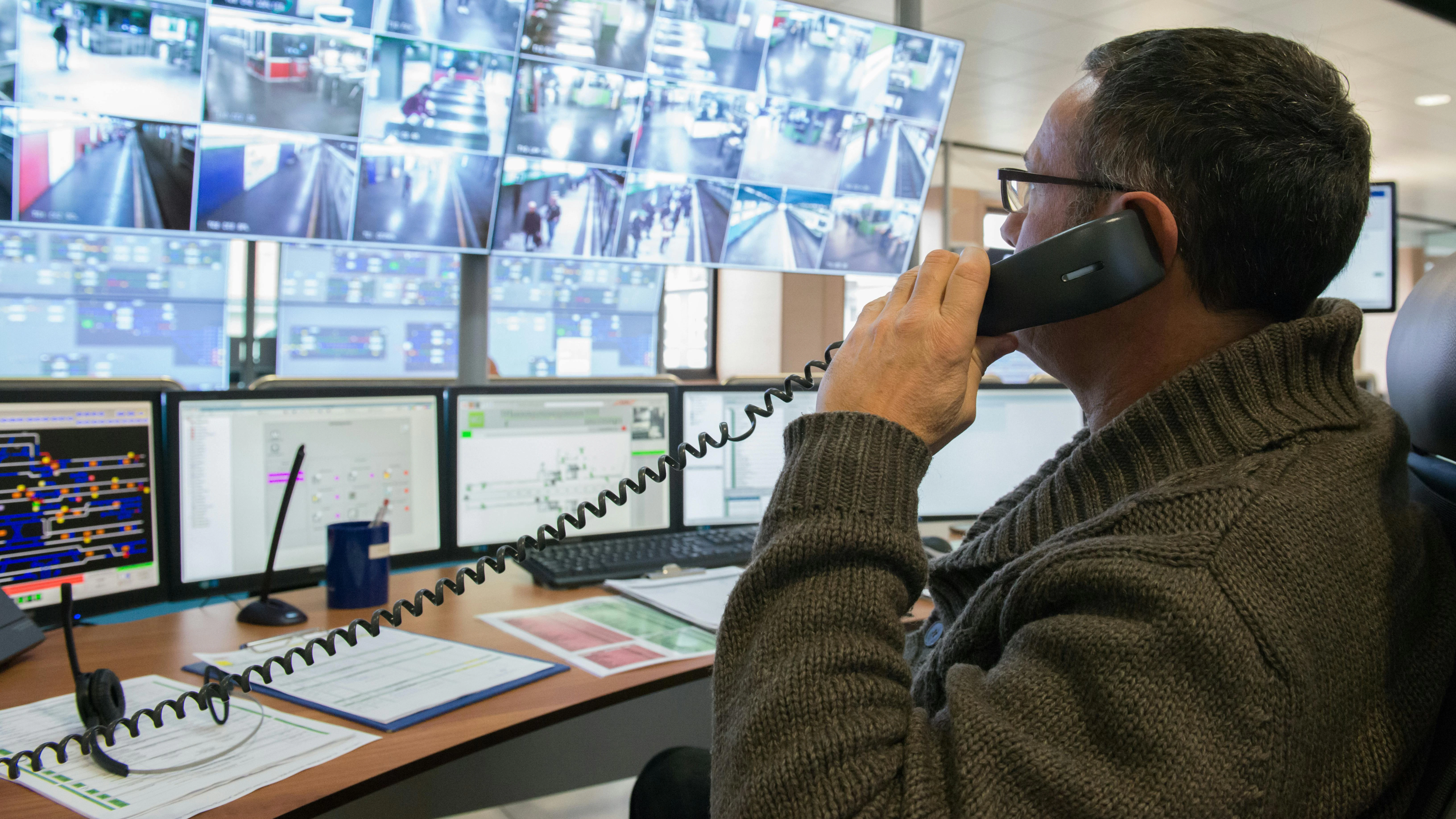 man on telephone in front of computer safety monitors in control room