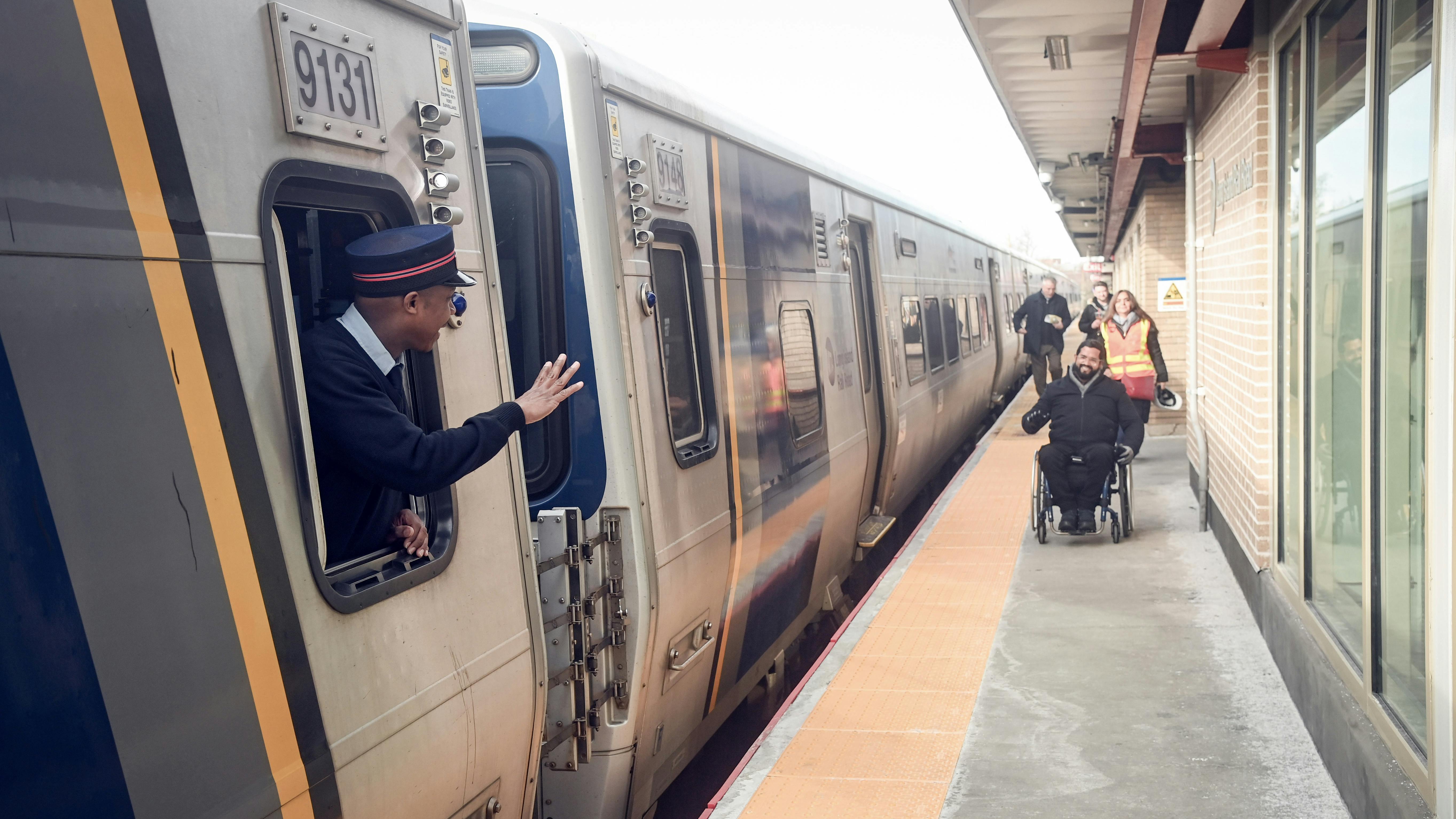 A conductor waves at a passenger in a wheelchair approaching the train at the newly upgraded Laurelton Station.