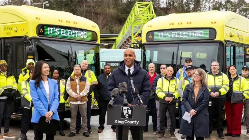 King County Metro leaders stand in front of the new buses parked angled in behind them.