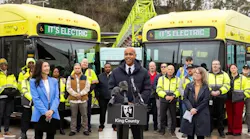 King County Metro leaders stand in front of the new buses parked angled in behind them.