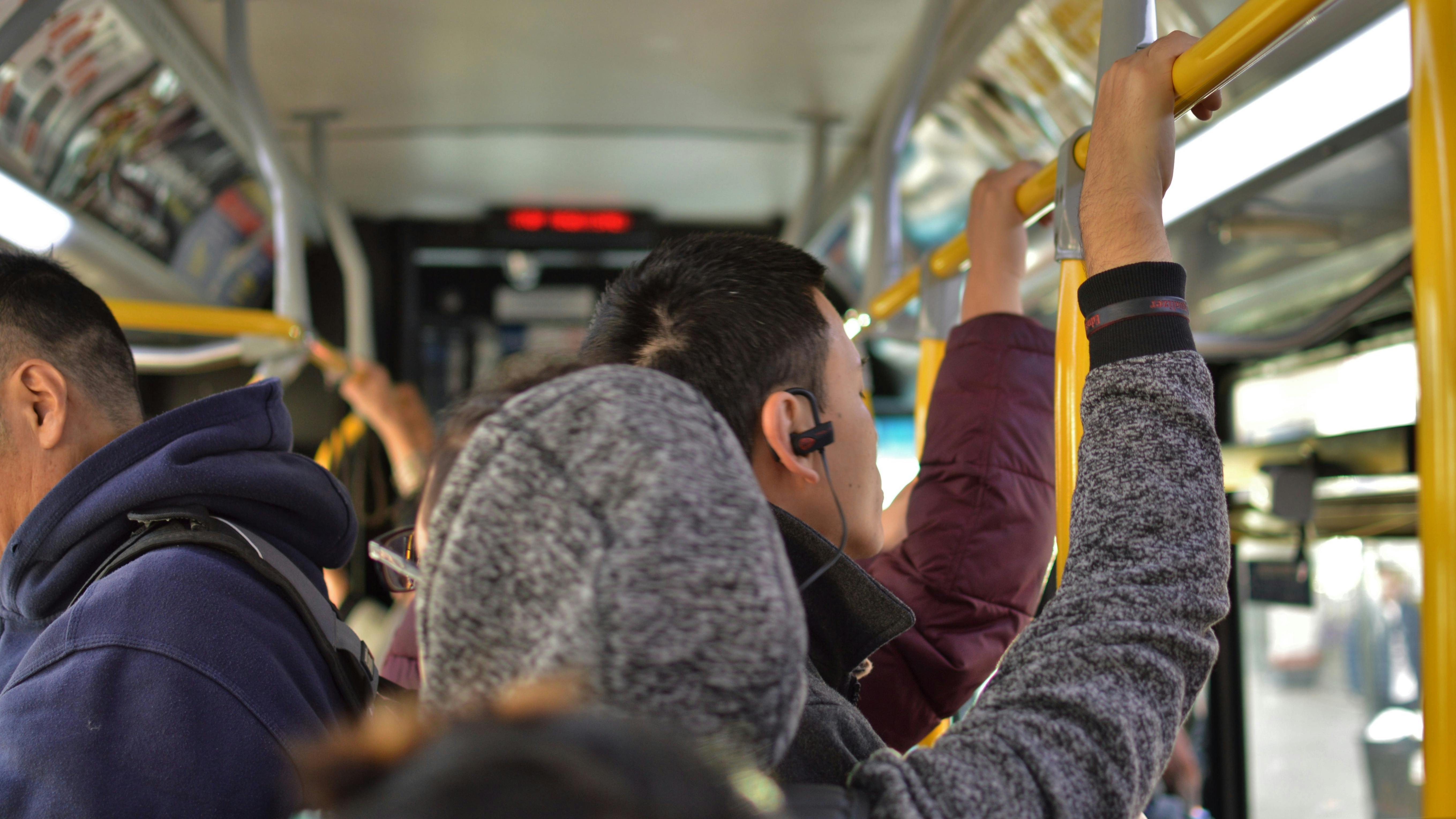 Commuters hold onto support poles on a bus.