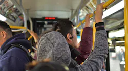 Commuters hold onto support poles on a bus.