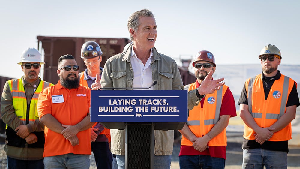 Gov. Newsom speaks at a podium in front of other CHSRA leaders and project managers.