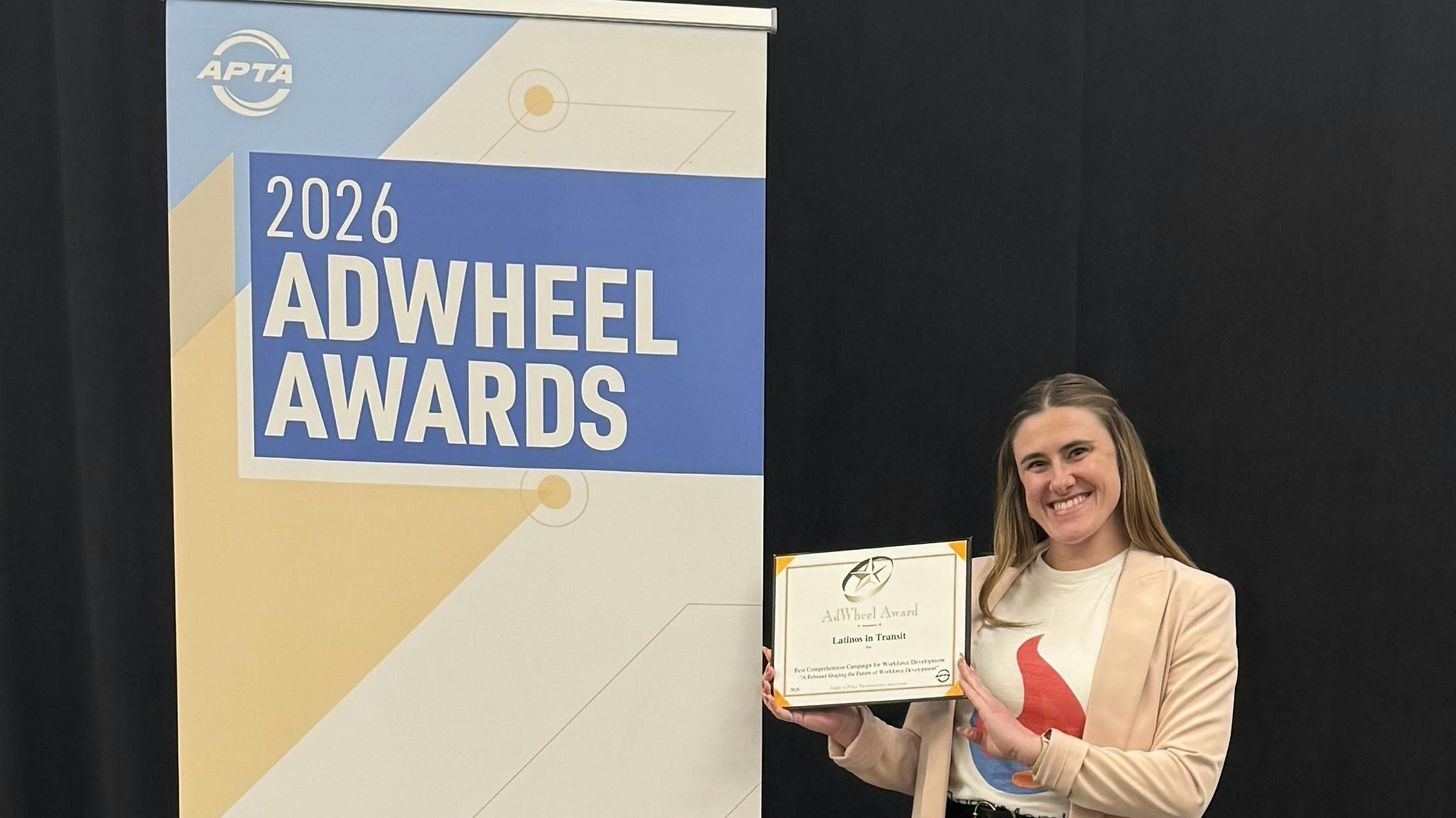 Megan Perrero, LIT Marketing and Communications Committee Chair, holds the award next to a 2026 AdWheel Awards banner.