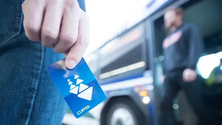 The image shows someone holding a clipper fare card with a person standing in the background blurred out due to focal length.