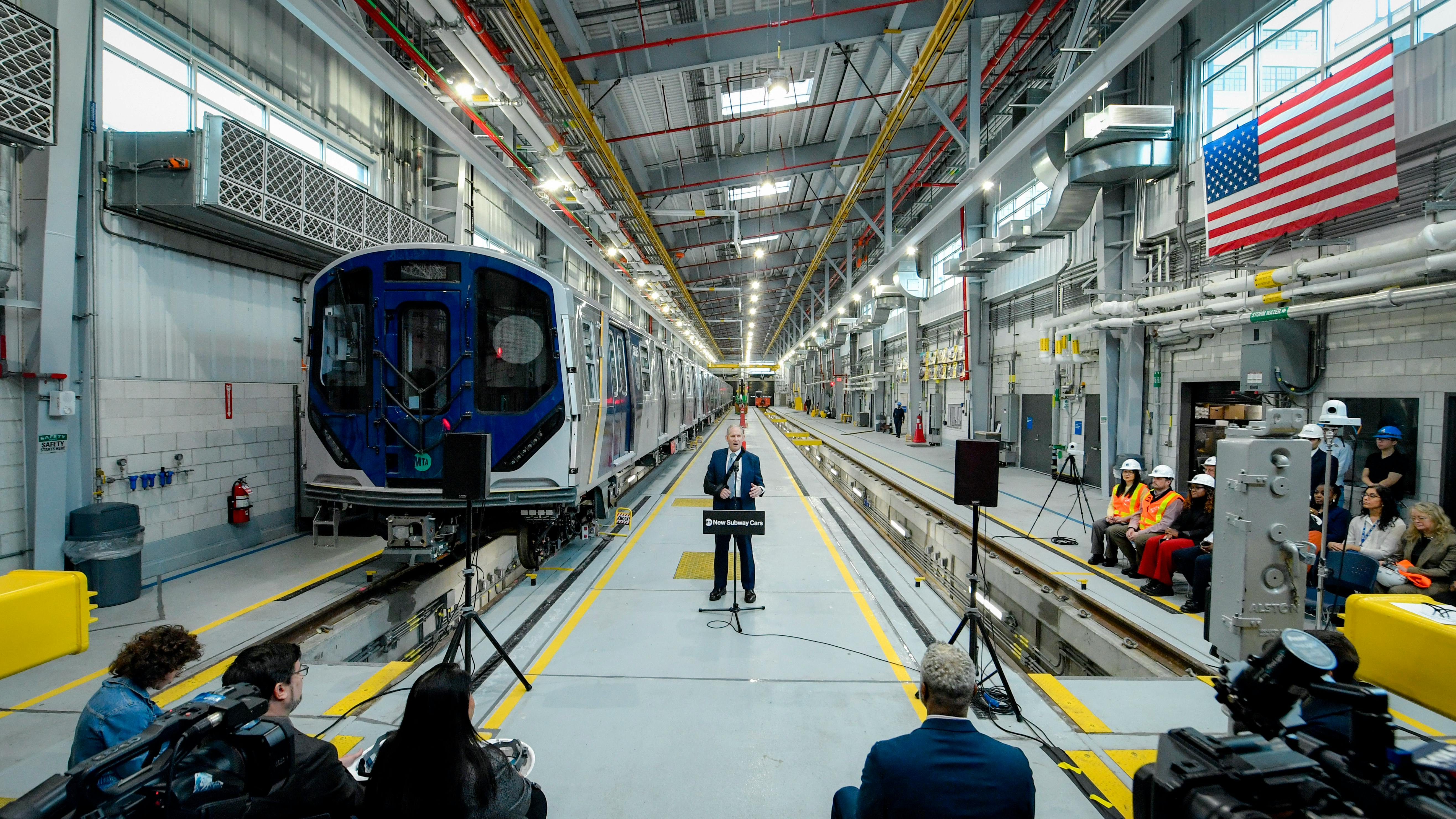 The image shows a wide shot of MTA CEO Jano Lieber speaking to event attendees from a lectern.