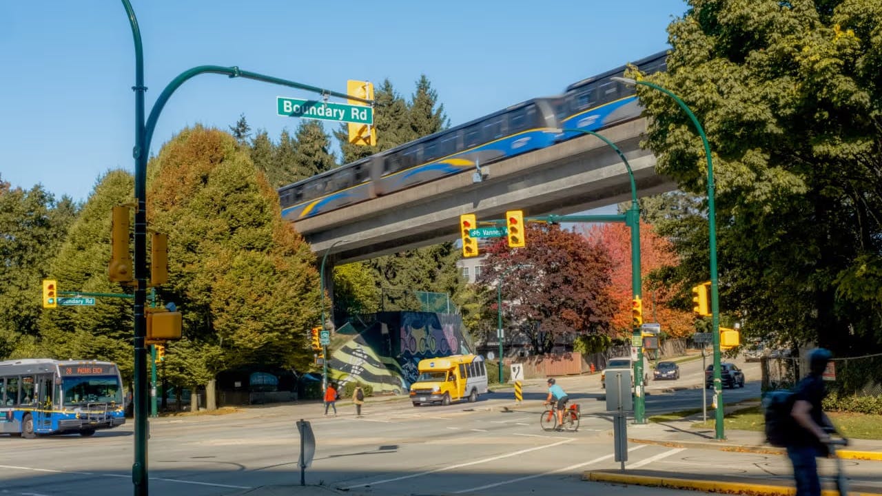 The image displays a bustling corner of Boundary Road, showing cars, a bus and an elevated train traversing through the scene.