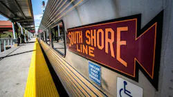 A Northern Indiana Commuter Transportation District South Shore Line commuter rail car sits at a station platform. The stainless steel car bears a maroon and orange 'South Shore Line' herald. A blue placard reads 'This car is not toilet equipped,' and an accessibility symbol is visible below it. The yellow tactile warning strip lines the platform edge. A Northern Indiana Commuter Transportation District South Shore Line commuter rail car sits at a station platform. The stainless steel car bears a maroon and orange 'South Shore Line' herald. A blue placard reads 'This car is not toilet equipped,' and an accessibility symbol is visible below it. The yellow tactile warning strip lines the platform edge.
