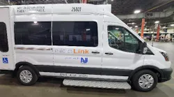 A New Jersey Transit MicroLink van, vehicle number 25801, photographed inside a maintenance facility. The white Ford Transit-based cutaway van displays the MicroLink branding and NJ Transit logo on its side, along with an accessibility symbol indicating wheelchair accessibility. A fold-out entry step is visible below the side door.