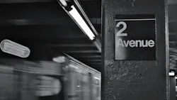 A black-and-white photo of a New York City subway platform column bearing a '2 Avenue' station sign, with a motion-blurred train passing in the background. Fluorescent lights run along the low ceiling above the platform. A black-and-white photo of a New York City subway platform column bearing a '2 Avenue' station sign, with a motion-blurred train passing in the background. Fluorescent lights run along the low ceiling above the platform.