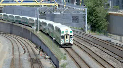 A GO Transit bi-level commuter rail train approaches on a curved, multi-track corridor in downtown Toronto, with the Concord CityPlace development visible in the background. A yellow signal gantry spans the tracks overhead, and several additional parallel tracks are visible in the foreground. A GO Transit bi-level commuter rail train approaches on a curved, multi-track corridor in downtown Toronto, with the Concord CityPlace development visible in the background. A yellow signal gantry spans the tracks overhead, and several additional parallel tracks are visible in the foreground.