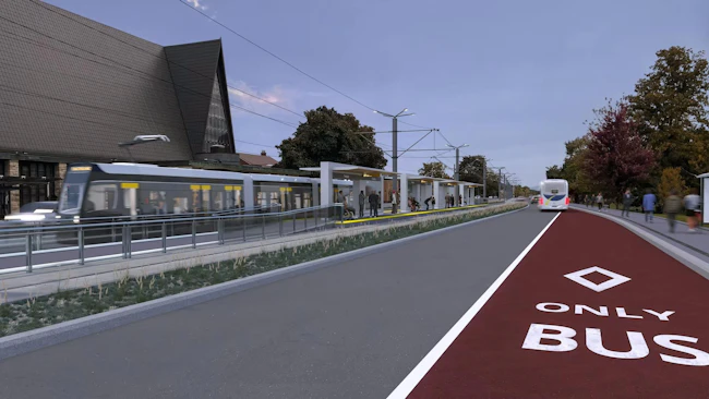 An architectural rendering of a surface light rail station at dusk, showing a modern low-floor train passing through with passengers waiting on a center platform beneath a canopy structure. A dedicated red bus-only lane runs parallel to the LRT corridor in the foreground, with a bus visible farther down the road. A stone church with a steep gabled roof anchors the left side of the image, and trees line the right side of the corridor..