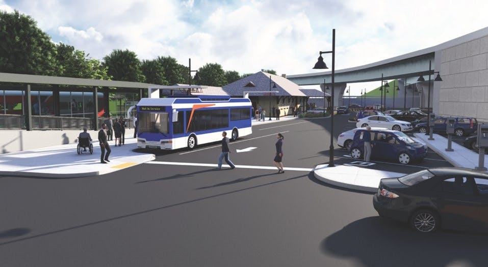 An architectural rendering of a transit hub showing a blue-and-white bus marked 'Not In Service' pulling through a passenger drop-off area. A historic station building with a peaked roof sits in the background, flanked by a modern covered bus shelter on the left and a parking lot on the right. Pedestrians and a wheelchair user are depicted on the sidewalk.