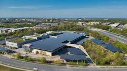 Aerial view of the David F. Bone Equipment Maintenance and Transit Operations Center in Montgomery County, Maryland. The large facility features an extensive solar panel array covering the bus storage canopies and maintenance building rooftop. A green roof is visible on one section of the building. The complex sits adjacent to a multilane highway, with a suburban landscape of trees and low-rise development visible in the background. Aerial view of the David F. Bone Equipment Maintenance and Transit Operations Center in Montgomery County, Maryland. The large facility features an extensive solar panel array covering the bus storage canopies and maintenance building rooftop. A green roof is visible on one section of the building. The complex sits adjacent to a multilane highway, with a suburban landscape of trees and low-rise development visible in the background.