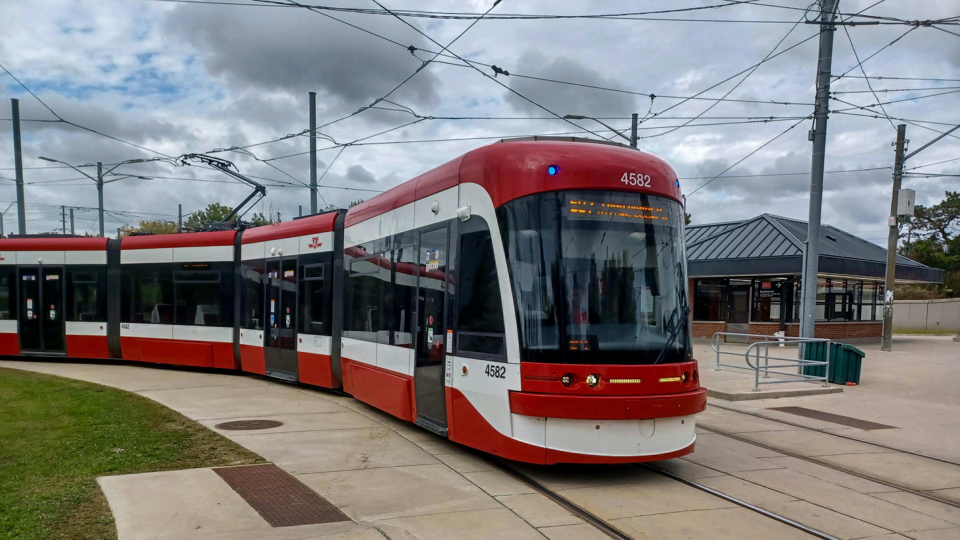 A Toronto Transit Commission (TTC) Bombardier Flexity Outlook streetcar, numbered 4582, curves along an outdoor track at what appears to be a terminal loop. The vehicle is painted in TTC's red and white livery. Overhead catenary wires are visible against a partly cloudy sky. A low transit station building is visible in the background at right.