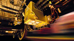 A close-up, low-angle view of a yellow electronic control unit mounted beneath a rail vehicle in motion. The unit, labeled with 'BCD' and 'PB1,' is surrounded by wiring and hydraulic lines. The background is blurred with streaks of color, suggesting the vehicle is traveling at speed. A close-up, low-angle view of a yellow electronic control unit mounted beneath a rail vehicle in motion. The unit, labeled with 'BCD' and 'PB1,' is surrounded by wiring and hydraulic lines. The background is blurred with streaks of color, suggesting the vehicle is traveling at speed.