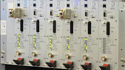 A rack of six AFTC5 train control modules mounted side by side in an equipment cabinet. Each module features labeled indicator lights for track circuit and communication status, USB and Ethernet ports, application key slots, and a program connector. Several units have yellow and green LEDs illuminated. Red-handled circuit breakers are visible at the bottom of each module. A rack of six AFTC5 train control modules mounted side by side in an equipment cabinet. Each module features labeled indicator lights for track circuit and communication status, USB and Ethernet ports, application key slots, and a program connector. Several units have yellow and green LEDs illuminated. Red-handled circuit breakers are visible at the bottom of each module.