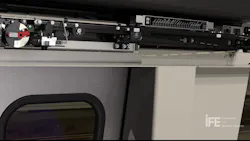 A cutaway product rendering showing the overhead door drive mechanism for a rail vehicle entrance system, branded by IFE (Innovations for Entrance Systems). The top panel reveals the linear motor track, roller assemblies, and a red-labeled emergency manual release mechanism. The lower portion shows the exterior of a closed sliding door with a small porthole window. The IFE logo appears in the lower right corner. A cutaway product rendering showing the overhead door drive mechanism for a rail vehicle entrance system, branded by IFE (Innovations for Entrance Systems). The top panel reveals the linear motor track, roller assemblies, and a red-labeled emergency manual release mechanism. The lower portion shows the exterior of a closed sliding door with a small porthole window. The IFE logo appears in the lower right corner.