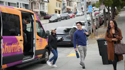 Passengers board and disembark from a purple and orange Bayview Shuttle van on a residential street in San Francisco's Bayview neighborhood. A street sign for Mendell Street is visible in the background. Passengers board and disembark from a purple and orange Bayview Shuttle van on a residential street in San Francisco's Bayview neighborhood. A street sign for Mendell Street is visible in the background.