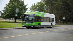 A BC Transit electric bus numbered 7503 travels along a two-lane road with a grassy median and tree line behind it. The bus is white with a bright green front and roof, which features rooftop equipment consistent with a battery-electric or overhead-charging system. The destination sign reads 'Welcome Aboard.' The front carries a bike rack and BC Transit branding. A BC Transit electric bus numbered 7503 travels along a two-lane road with a grassy median and tree line behind it. The bus is white with a bright green front and roof, which features rooftop equipment consistent with a battery-electric or overhead-charging system. The destination sign reads 'Welcome Aboard.' The front carries a bike rack and BC Transit branding.