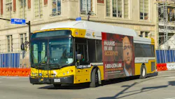 A yellow and white Dallas Area Rapid Transit bus, fleet number 42016, travels through a downtown Dallas intersection at the 400-500 block of Main Street. The bus carries a full-side advertisement for a personal injury law firm. Orange construction barriers and chain-link fencing line the street, and a multi-story building is visible in the background. A yellow and white Dallas Area Rapid Transit bus, fleet number 42016, travels through a downtown Dallas intersection at the 400-500 block of Main Street. The bus carries a full-side advertisement for a personal injury law firm. Orange construction barriers and chain-link fencing line the street, and a multi-story building is visible in the background.
