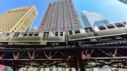 A Chicago Transit Authority elevated rail train passes through the Loop on the iconic 'L' structure, photographed from street level against a clear blue sky with downtown skyscrapers rising in the background.