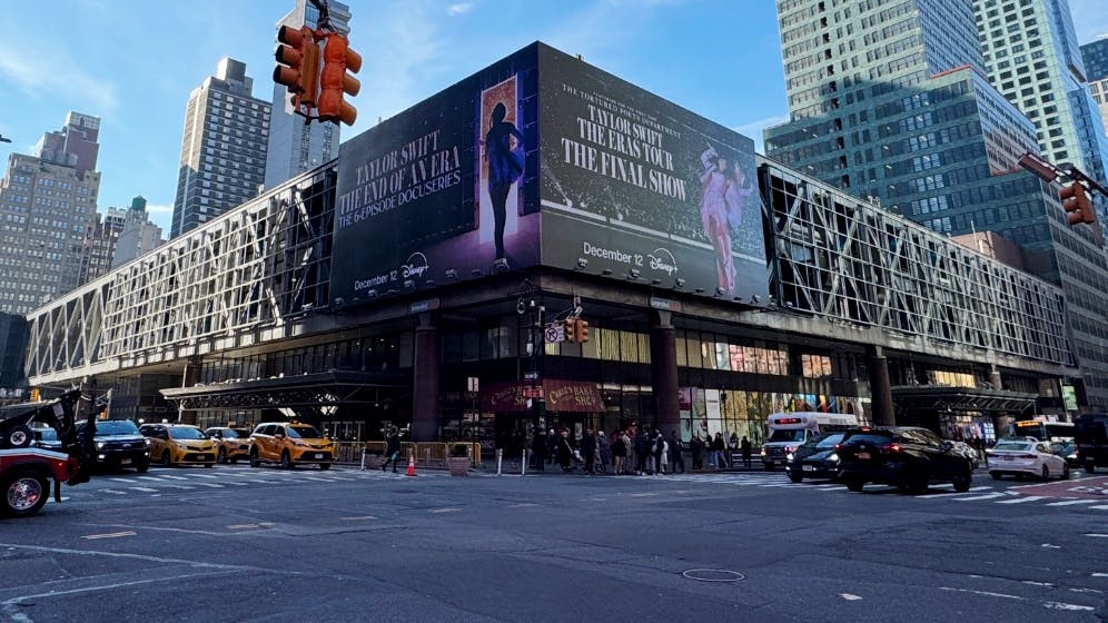The exterior of the Port Authority Bus Terminal in Midtown Manhattan, viewed from street level at the intersection of Eighth Avenue and 42nd Street, with yellow taxis and pedestrians visible along the sidewalk.