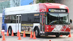 A Utah Transit Authority compressed natural gas bus, number 25001, navigates an orange traffic cone course during the APTA International Bus Roadeo competition. The red, white and blue bus displays a Markosian Auto advertisement on its side and shows Route 101 Marcus heading on its destination sign. A Utah Transit Authority compressed natural gas bus, number 25001, navigates an orange traffic cone course during the APTA International Bus Roadeo competition. The red, white and blue bus displays a Markosian Auto advertisement on its side and shows Route 101 Marcus heading on its destination sign.