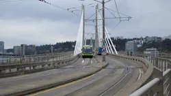 A green TriMet FX articulated bus crosses the cable-stayed Tilikum Crossing bridge in Portland, Oregon, sharing the transit-only deck with light rail tracks, with the city skyline and overcast sky in the background. A green TriMet FX articulated bus crosses the cable-stayed Tilikum Crossing bridge in Portland, Oregon, sharing the transit-only deck with light rail tracks, with the city skyline and overcast sky in the background.