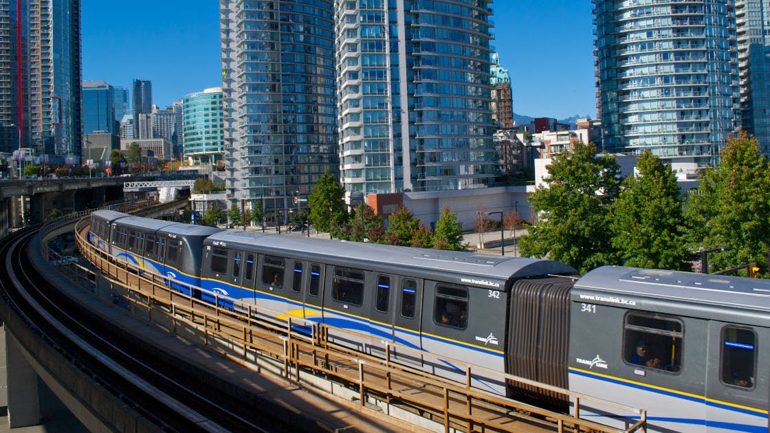 A TransLink SkyTrain traveling on an elevated guideway through downtown Vancouver.