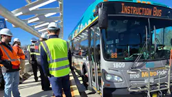 Denver RTD staff in hard hats and high-visibility vests gather alongside a teal and silver New Flyer Free MetroRide bus marked 'Instruction Bus' as it pulls up to a platform along the East Colfax Bus Rapid Transit corridor in Denver. Denver RTD staff in hard hats and high-visibility vests gather alongside a teal and silver New Flyer Free MetroRide bus marked 'Instruction Bus' as it pulls up to a platform along the East Colfax Bus Rapid Transit corridor in Denver.