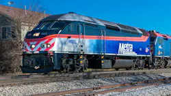 A Metra commuter rail locomotive numbered 422 in the agency's blue, silver and orange livery sits on track in front of a second Metra locomotive, with bare trees and a building behind under a clear blue sky. A Metra commuter rail locomotive numbered 422 in the agency's blue, silver and orange livery sits on track in front of a second Metra locomotive, with bare trees and a building behind under a clear blue sky.