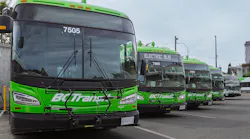 A row of bright green BC Transit battery-electric buses lined up at a transit yard, with the lead bus numbered 7505 in the foreground and additional units, including one with 'Electric Bus' on its destination sign, receding behind it.