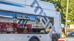 A white Metropolitan Atlanta Rapid Transit Authority bus with the agency's gray 'MARTA' logo wrap travels along an Atlanta street, with a passenger visible inside near a interior advertisement and a Wyman Street sign at right.