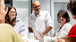 Five Alstom colleagues gather around a conference table in a bright office, with one man standing at the head holding a tablet as he speaks to the seated group over coffee cups. Five Alstom colleagues gather around a conference table in a bright office, with one man standing at the head holding a tablet as he speaks to the seated group over coffee cups.