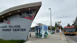 A free-standing Throne self-cleaning public restroom unit sits on the sidewalk at King County Metro's Aurora Village Transit Center, with the center's curved entrance signage at left and a red and yellow RapidRide E Line bus to downtown Seattle at a stop on the right. A free-standing Throne self-cleaning public restroom unit sits on the sidewalk at King County Metro's Aurora Village Transit Center, with the center's curved entrance signage at left and a red and yellow RapidRide E Line bus to downtown Seattle at a stop on the right.