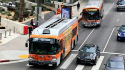 Two orange and silver LA Metro Local buses operate in downtown Los Angeles, with a Route 20 bus to Westwood stopped at a crosswalk in the foreground and a Route 16 bus to 6th-Los Angeles pulling up to a stop in the background, alongside cars on a multi-lane street. Two orange and silver LA Metro Local buses operate in downtown Los Angeles, with a Route 20 bus to Westwood stopped at a crosswalk in the foreground and a Route 16 bus to 6th-Los Angeles pulling up to a stop in the background, alongside cars on a multi-lane street.