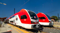 Two Caltrain trains sit next to each other at a station against a clear blue sky.