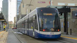 A blue and white Edmonton Transit Service Bombardier Flexity light rail vehicle pulls into a downtown Valley Line station, with workers in high-visibility vests on the platform and Edmonton's downtown skyline visible behind. A blue and white Edmonton Transit Service Bombardier Flexity light rail vehicle pulls into a downtown Valley Line station, with workers in high-visibility vests on the platform and Edmonton's downtown skyline visible behind.