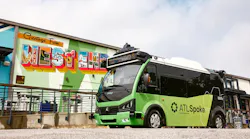 A green ATLSpoke autonomous shuttle from Beep sits parked in front of a colorful 'Greetings From West End' postcard-style mural in Atlanta's Westside neighborhood, with rooftop sensors and lidar equipment visible on the vehicle.