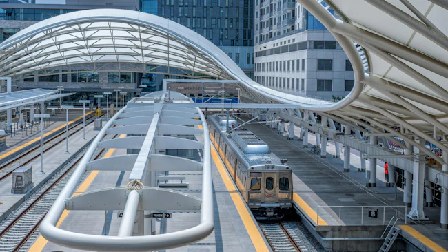 A two-car RTD commuter rail train sits at Denver Union Station's Track 8, with the station's distinctive curved white canopies arching overhead and downtown Denver high-rises visible behind.