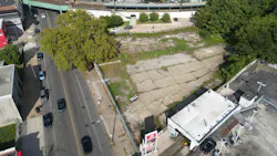 An aerial view of a vacant, cracked-pavement lot adjacent to the Germantown SEPTA Regional Rail station, with a large tree at one corner, neighboring commercial buildings and an elevated rail platform visible in the background. An aerial view of a vacant, cracked-pavement lot adjacent to the Germantown SEPTA Regional Rail station, with a large tree at one corner, neighboring commercial buildings and an elevated rail platform visible in the background.
