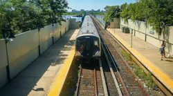 A new MTA R211 subway train enters Broad Channel station on the elevated Rockaway line as part of the Rockaway Park Shuttle's rolling stock upgrade, with Jamaica Bay marshland and a distant skyline behind.