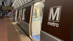 A Washington Metropolitan Area Transit Authority Metrorail train sits at an underground platform with an open door revealing the brightly lit interior, with the agency's 'M metro' wordmark on the brown side panels and the station's distinctive coffered concrete vault ceiling overhead. A Washington Metropolitan Area Transit Authority Metrorail train sits at an underground platform with an open door revealing the brightly lit interior, with the agency's 'M metro' wordmark on the brown side panels and the station's distinctive coffered concrete vault ceiling overhead.