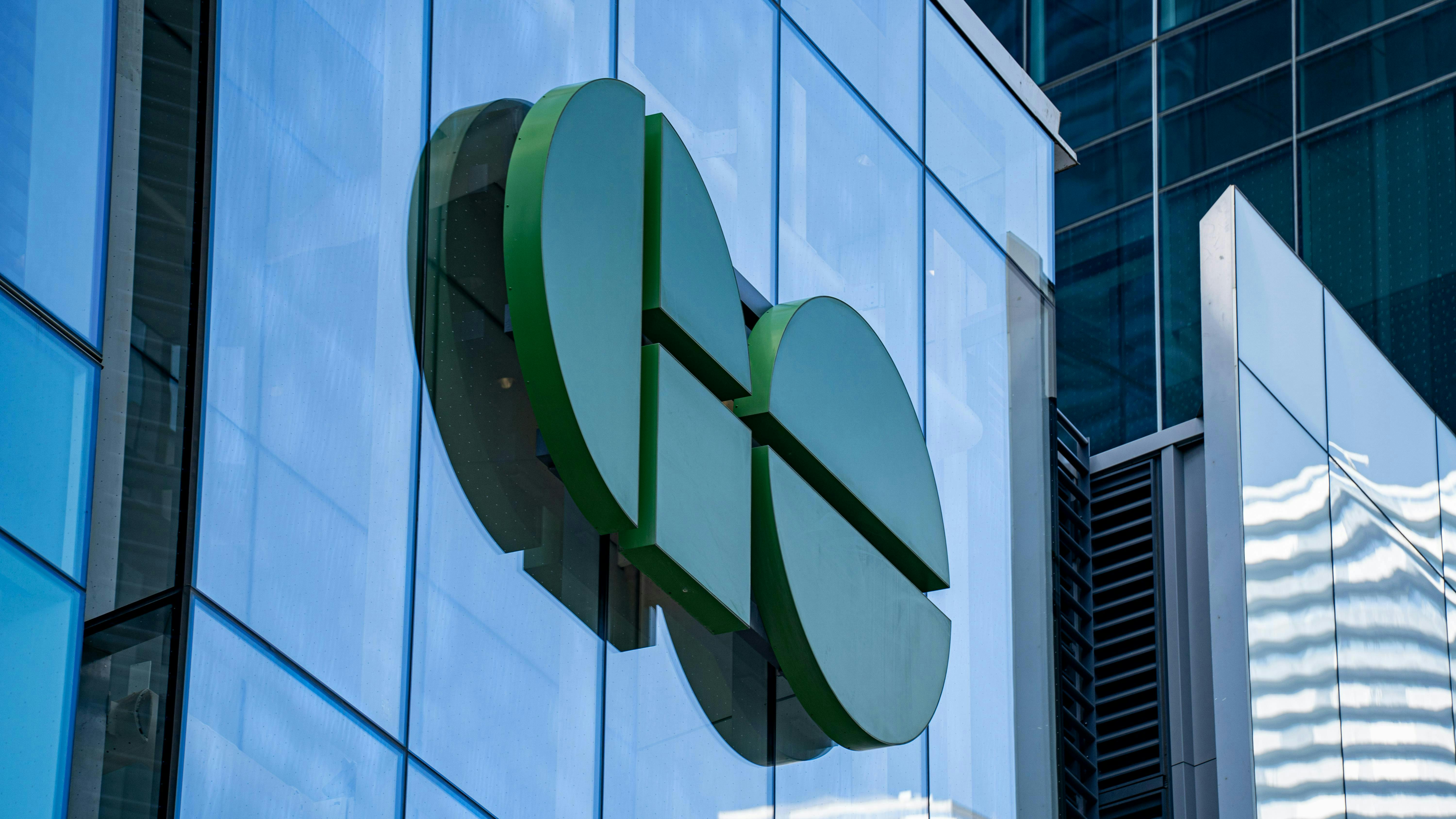 A large three-dimensional GO Transit logo mounted on the glass exterior of a modern office building, rendered in dark and light green tones against a blue-tinted glass curtain wall facade.