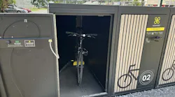 An open Velomodo secure bike locker at SEPTA's Fox Chase Regional Rail station reveals a bicycle stored inside, with an adjacent closed locker unit displaying the Velomodo logo, a bike icon and the number '02.'