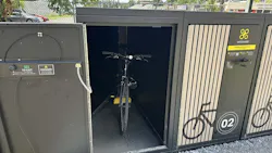 An open Velomodo secure bike locker at SEPTA's Fox Chase Regional Rail station reveals a bicycle stored inside, with an adjacent closed locker unit displaying the Velomodo logo, a bike icon and the number '02.'