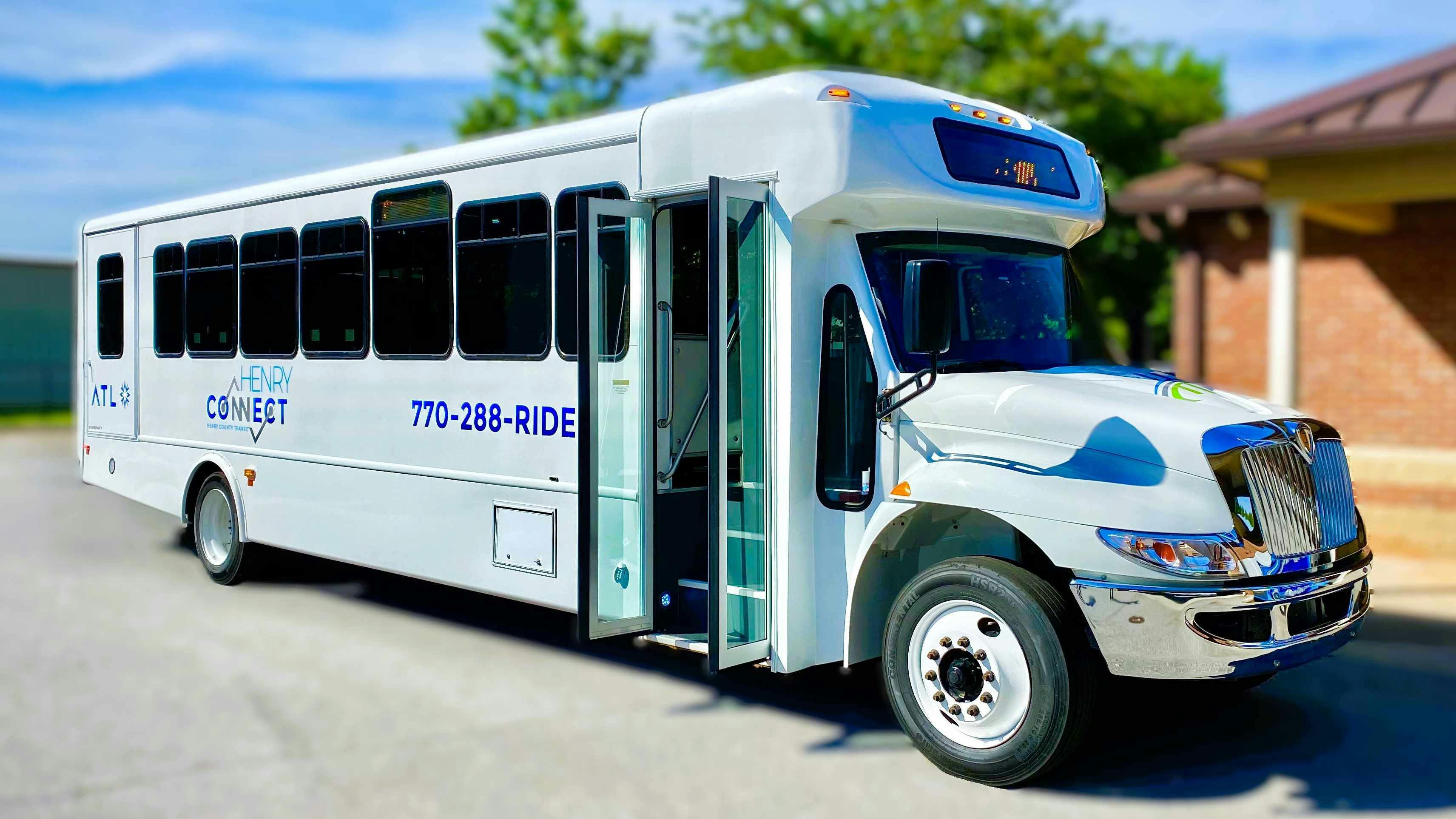 A new white Henry Connect cutaway bus operated by Henry County Transit, marked with ATL branding, the Henry Connect logo and the phone number 770-288-RIDE, sits parked with its front passenger door open, showing the low-floor entry step.