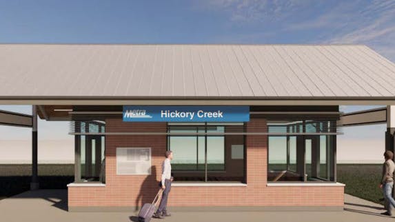 An architectural rendering of a new Metra Hickory Creek station building, featuring a low-pitched metal roof, brick base, large glass windows, and a blue Metra station sign, with two pedestrians depicted approaching the entrance.