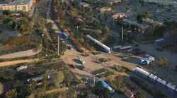 A rendering of Austin's future light rail line along Pleasant Valley Road, showing a modern white and blue light rail vehicle traveling alongside a landscaped multi-use path and roadway, with strip-mall retail and parking lots to the sides and the downtown Austin skyline in the distance at dusk.